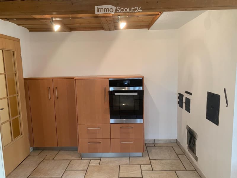 Modern kitchen with wooden cabinets, stainless steel oven, tiled floor, and a fireplace on the wall.