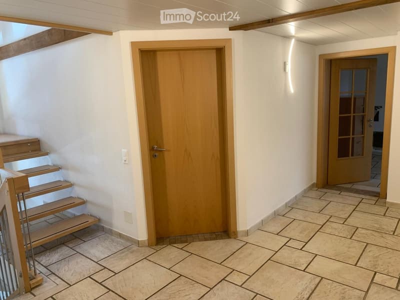 A clean, well-lit hallway with tiled flooring, wooden doors, and a staircase leading upwards.