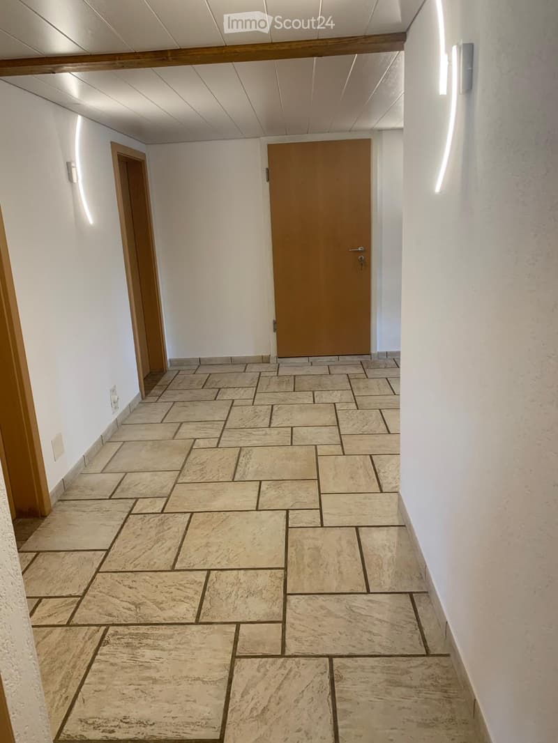 Empty hallway with tiled floor and white walls, featuring two wooden doors and a light fixture on the wall.