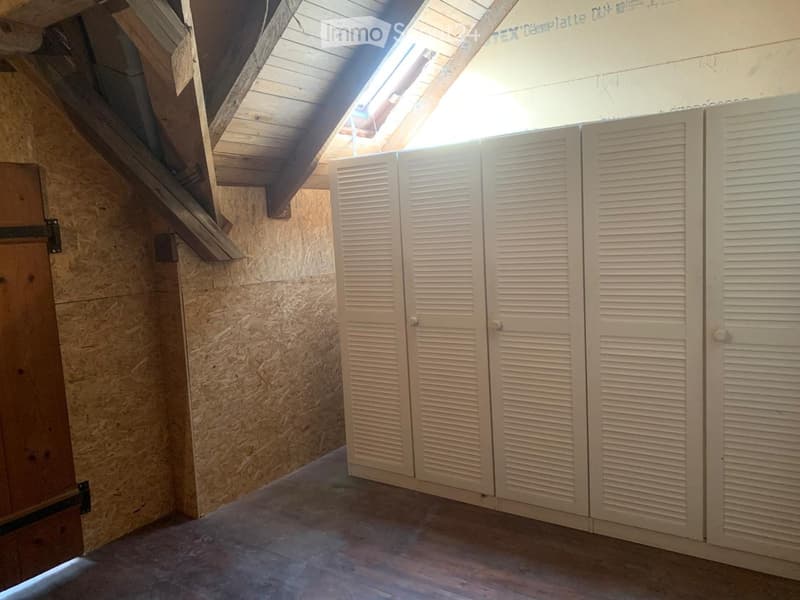 Empty attic space with exposed wooden beams, skylight, and white louvered shutters.