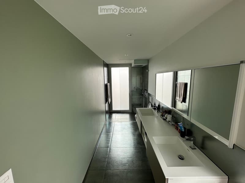 Modern bathroom with two sinks, large mirror, and a window leading to another room.