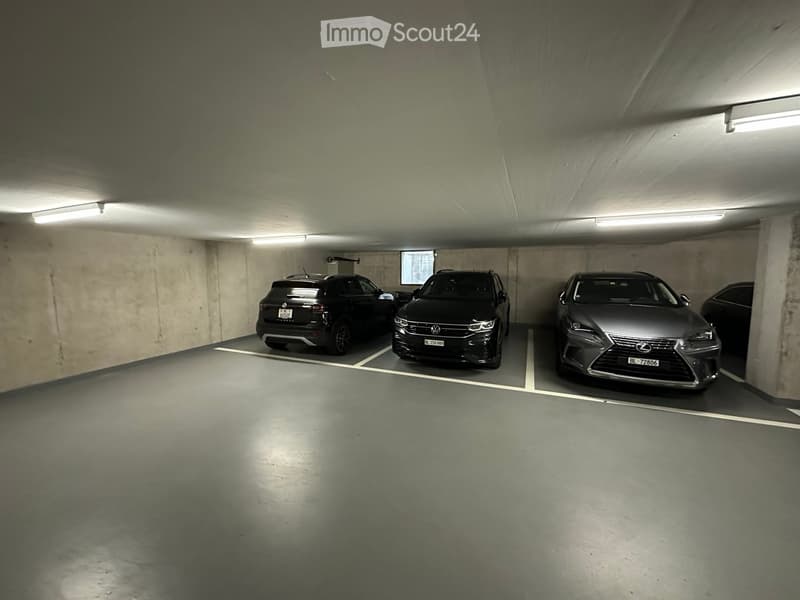 Underground parking area with four parked cars, concrete walls, and fluorescent lighting.