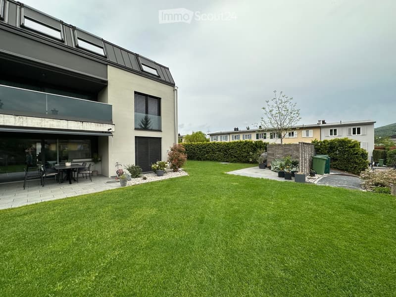 Well-maintained garden with a large lawn, patio area with outdoor furniture, and modern house with large windows and a balcony.