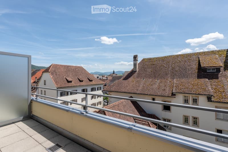 Balcony with metal railing overlooking a town with traditional houses and tiled roofs under a clear blue sky.