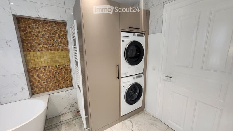 Modern bathroom with a bathtub, mosaic tile shower wall, and stacked washer/dryer unit.
