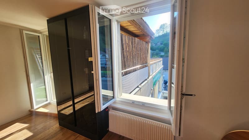Open sliding doors lead to a small balcony with wooden decking, overlooking a wooden fence and neighboring rooftops.
