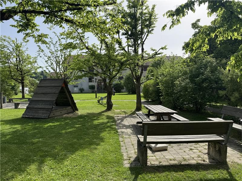 A well-maintained garden area with a wooden playhouse, picnic table, benches, and trees providing shade.