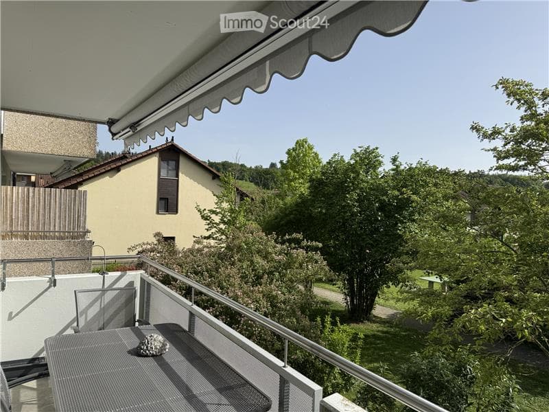 Balcony with metal railing, awning, and scenic view of a house and greenery.