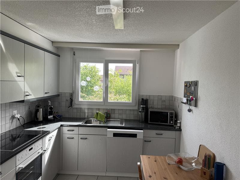 Modern kitchen with white cabinets, stainless steel appliances, and a wooden dining table with a bowl and cup on it.