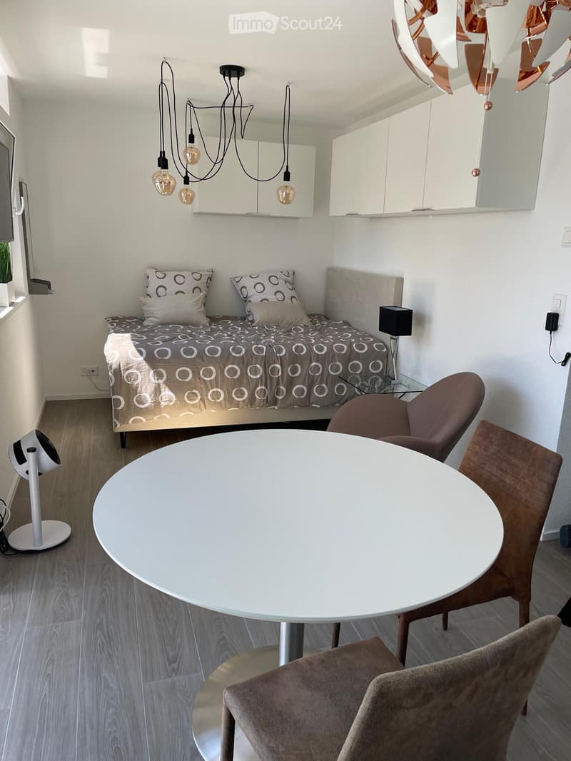 bedroom with double bed, nightstands with lamps, round dining table, 3 chairs, white walls, hanging lamp