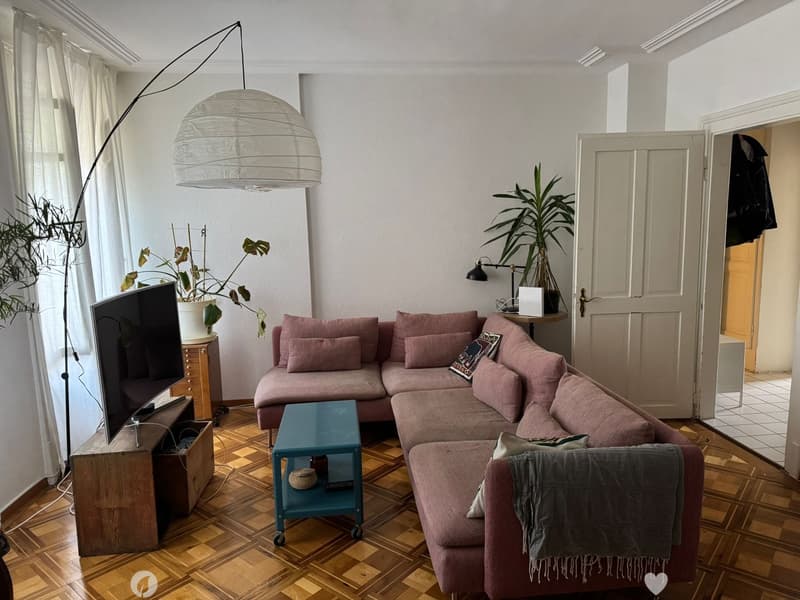 Modern living room with a pink sectional sofa, coffee table, TV, floor lamp, side table, and plants.