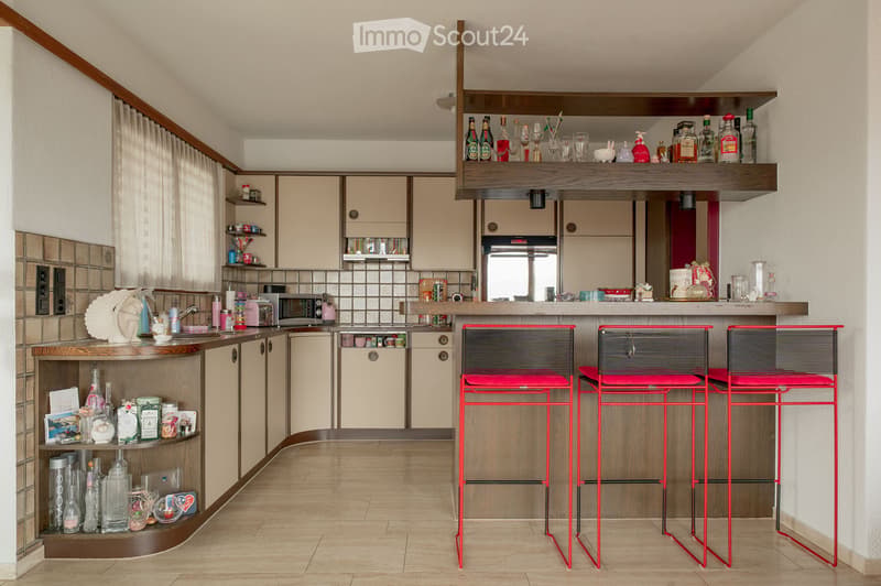 Modern kitchen with light wood cabinets, stainless steel appliances, and a central island with three red stools.
