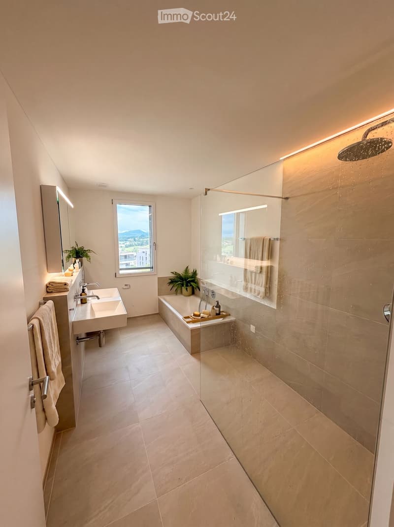 Modern bathroom with a large window offering a scenic view, featuring a double sink, bathtub, shower, and decorative plants.