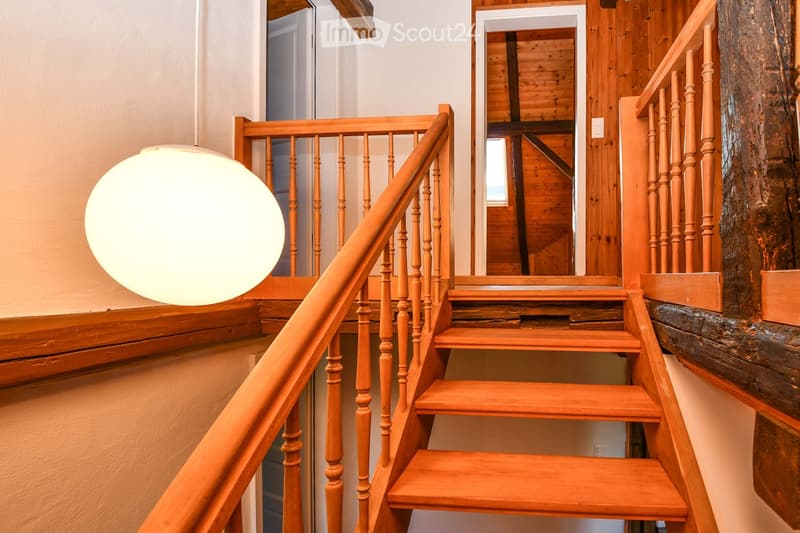 Wooden staircase with a handrail and balusters, a large spherical light fixture on the left, and a view into another room with wooden walls and a mirror.