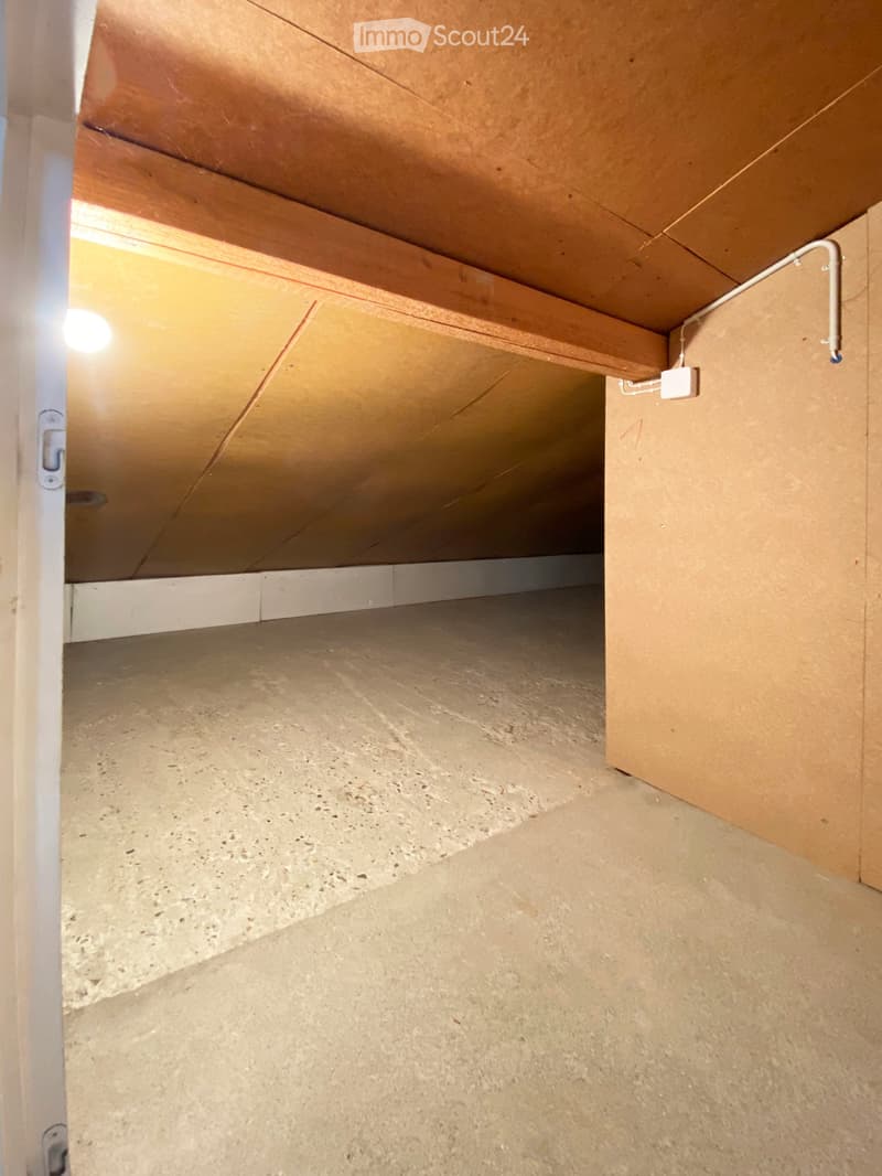Empty attic space with exposed wooden beams, concrete floor, and visible wiring. No furniture or equipment present.