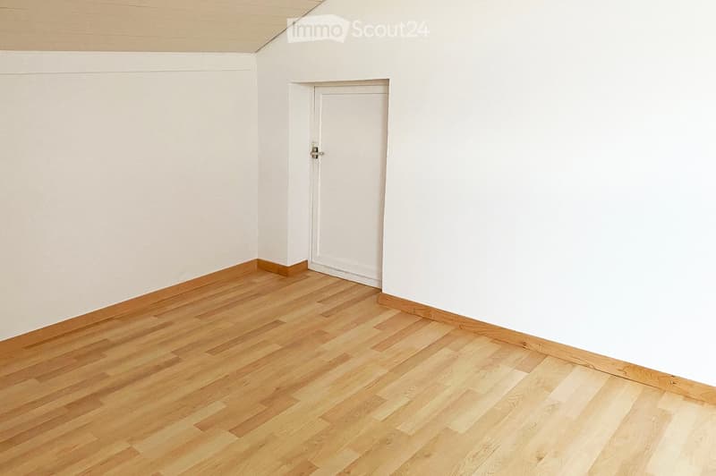 Empty room with light wooden flooring and white walls, featuring a single white door.