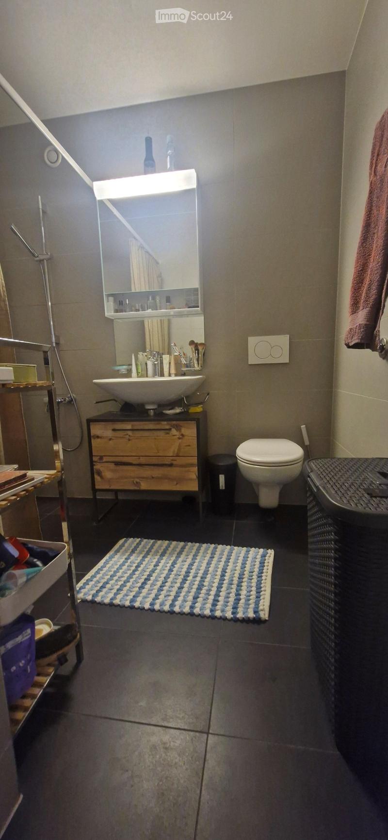 Modern bathroom with dark tiled floor, wooden cabinet, sink, mirror, toilet, and a blue and white striped rug.