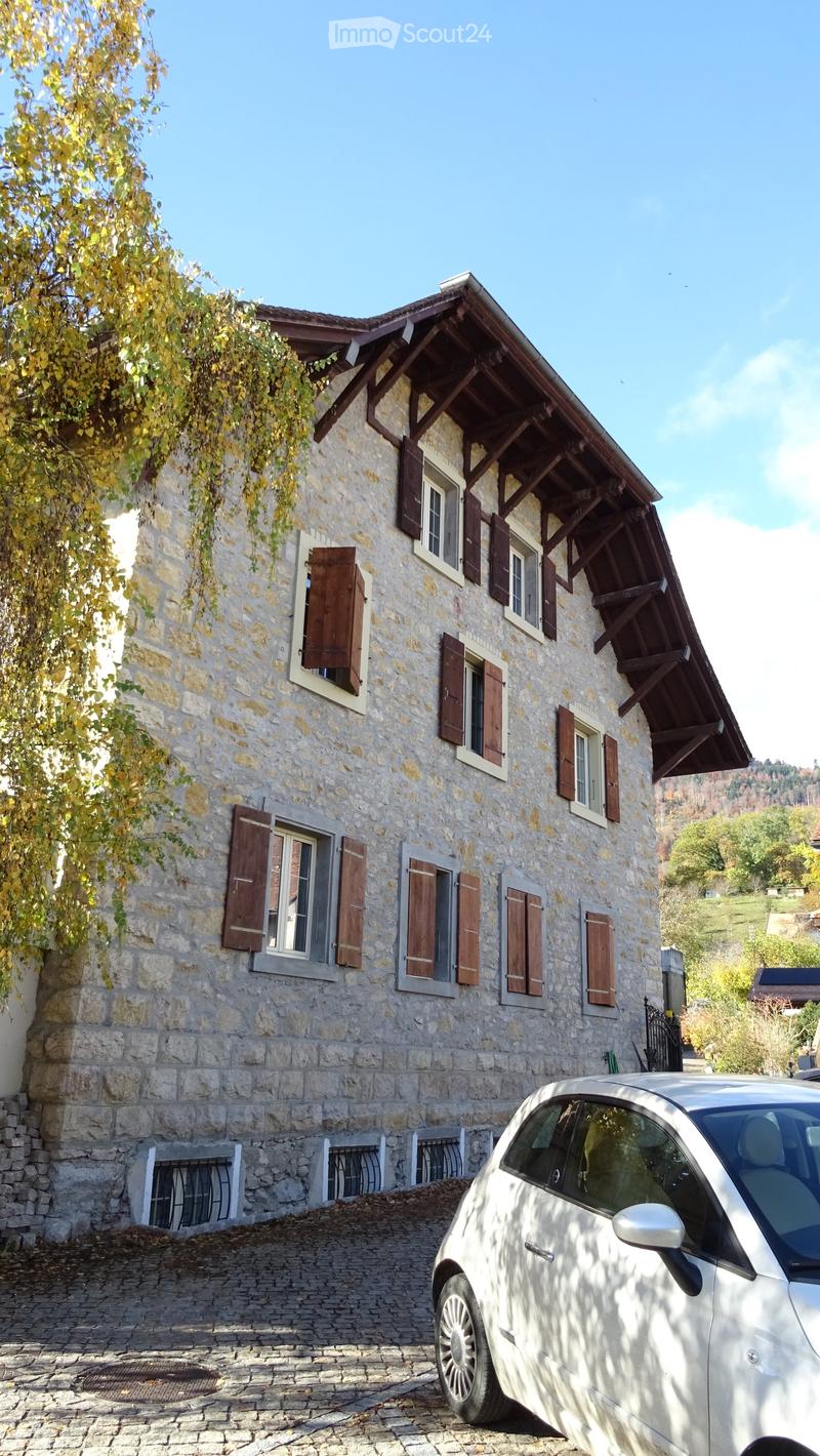 2-story stone house, wooden shutters, sloping roof, stone driveway, car in front
