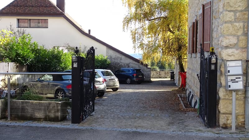 Three cars parked in driveway behind closed gates with stone walls on either side.