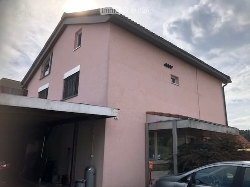 Two-story house with light pink exterior, multiple windows, garage, and a small balcony area.