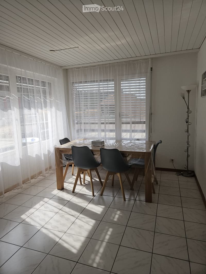 Bright kitchen with tiled floor, large windows with blinds and sheer curtains, dining table with four chairs, and a floor lamp near the window.