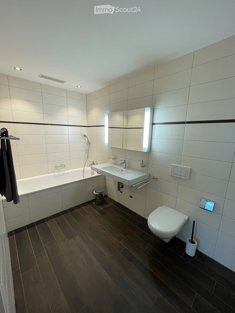 modern bathroom with white tiles, bathtub, white sink, white toilet, dark wooden flooring