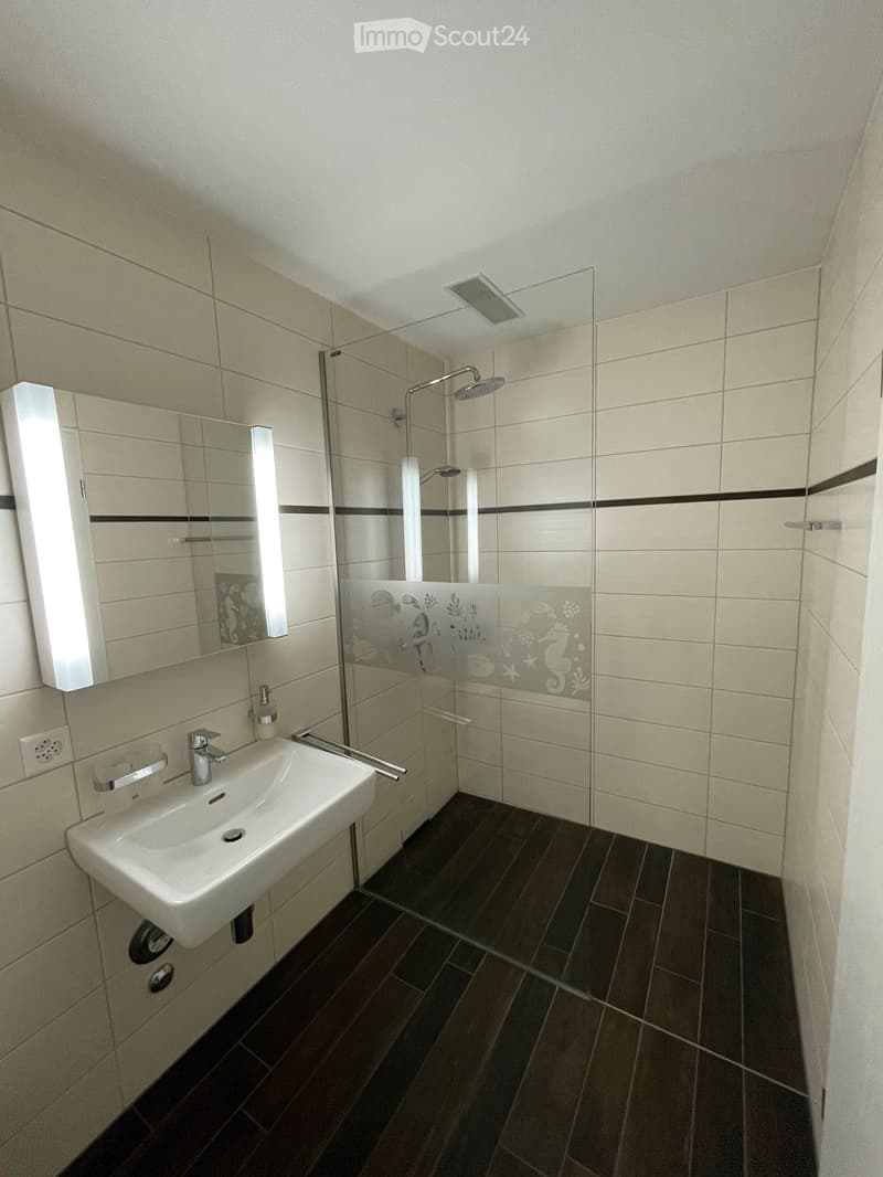 modern bathroom with a white sink, mirror, glass shower, white tiled walls, wooden floor