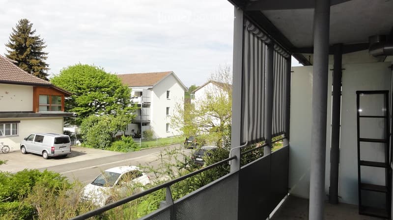 Balcony overlooking a residential street with parked cars, houses, and greenery.