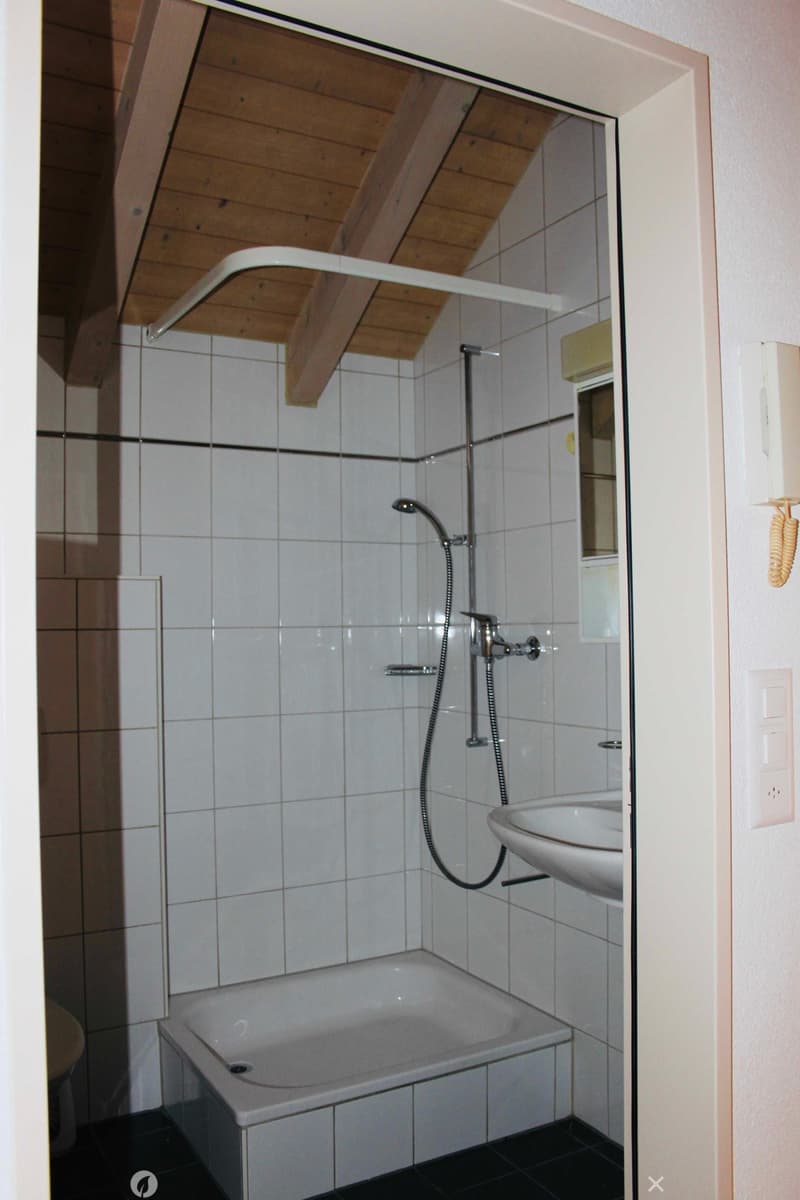 A small white tiled bathroom with a shower, sink, and toilet.