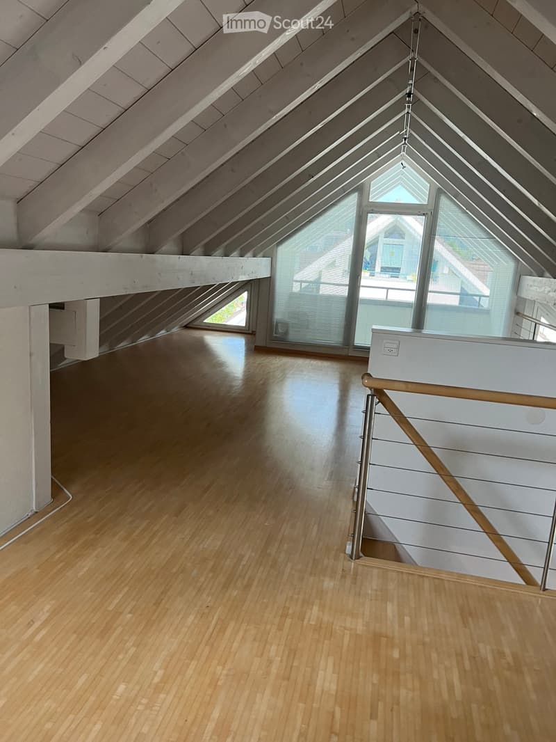 Empty attic space with wooden flooring, white walls, and a modern staircase leading upwards. Large skylight and windows provide natural light.
