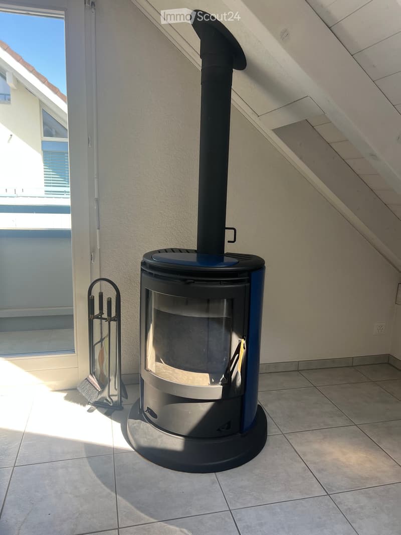 Modern wood-burning stove with a chimney, fireplace tools nearby, and tiled flooring.