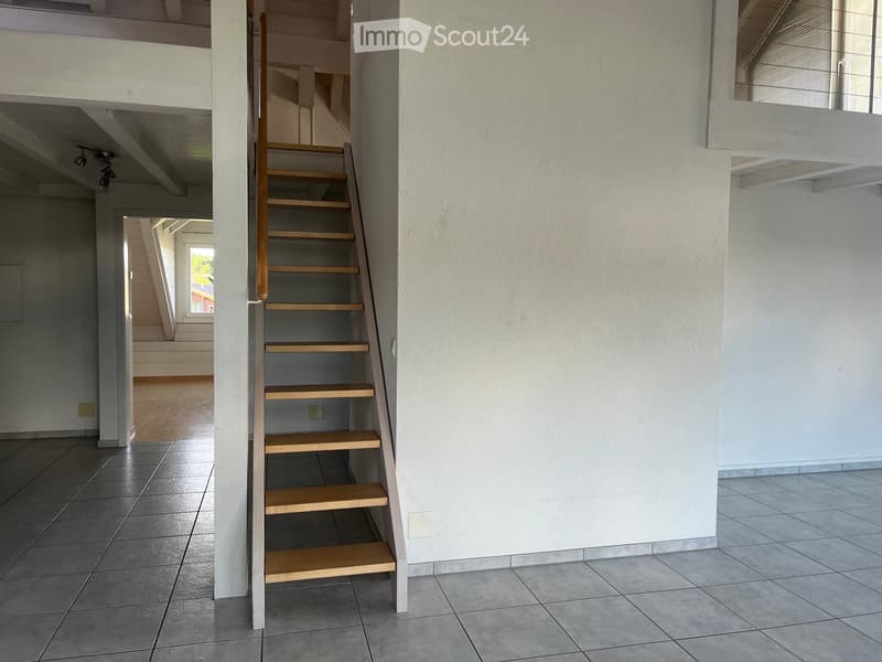 Modern hallway with a wooden staircase leading to an upper level, tiled floor, white walls, and a view of another staircase in the background.