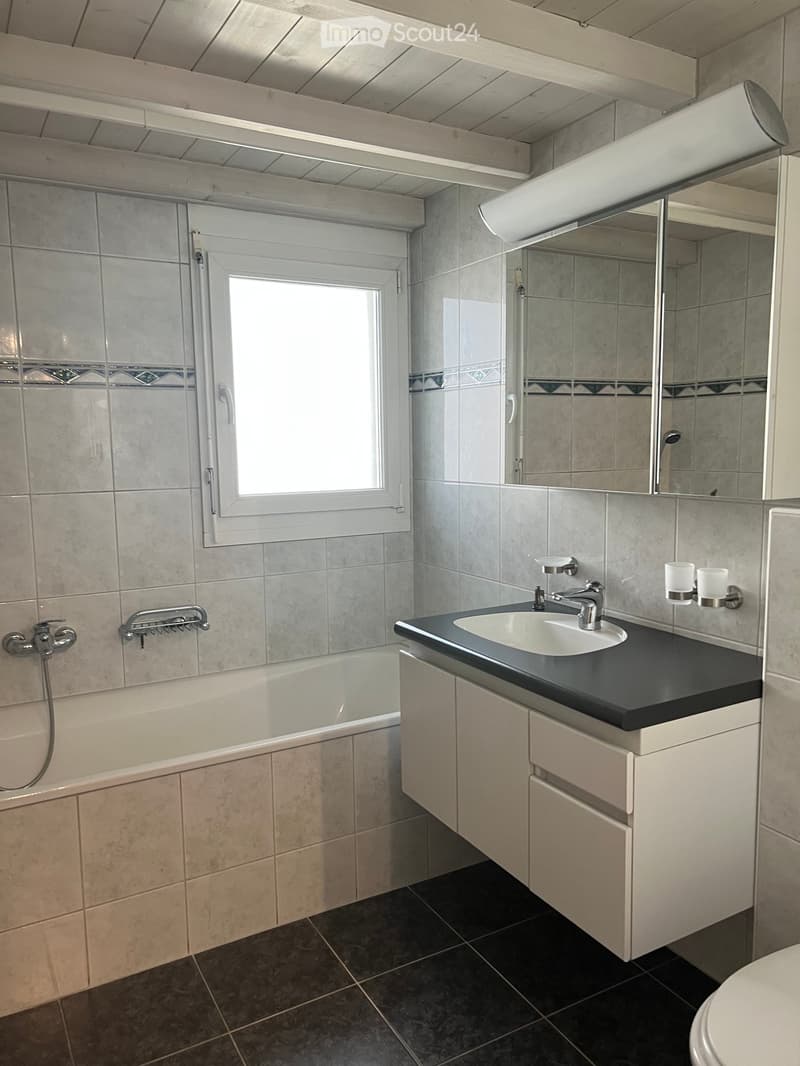 Modern bathroom with a bathtub, sink, mirror, and cabinet. Features tiled walls and a window for natural light.