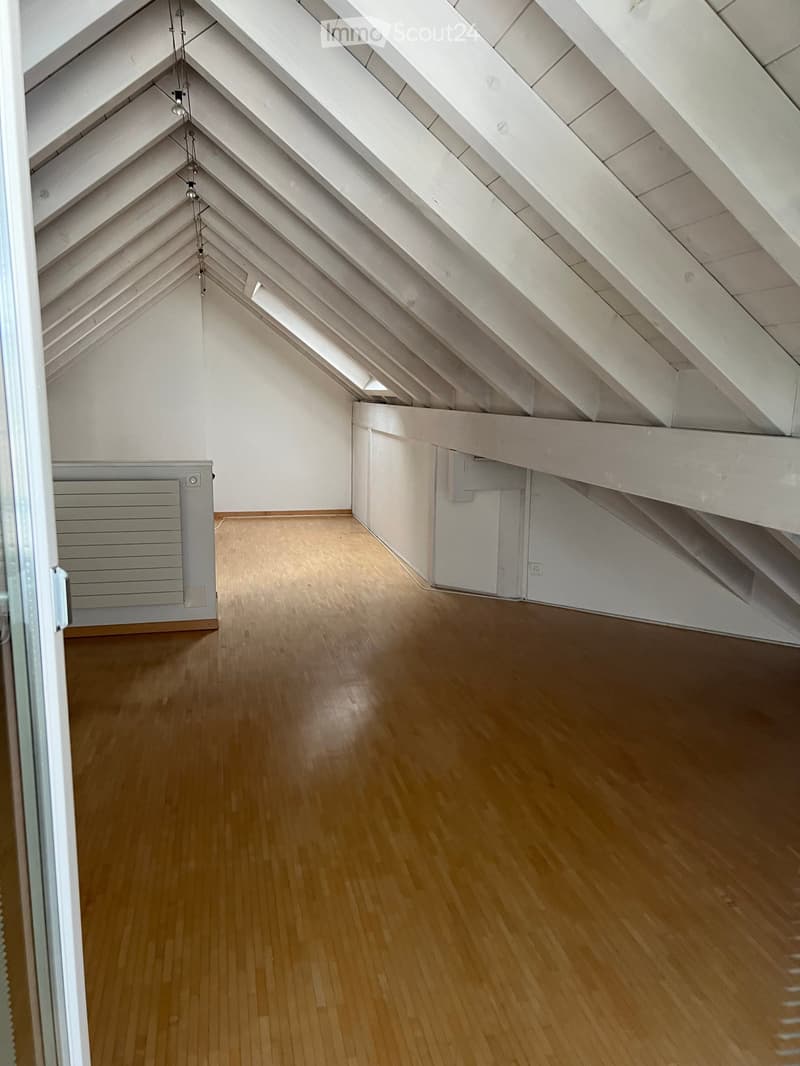 Empty attic space with wooden flooring, white walls, and exposed wooden beams on the ceiling. No furniture or equipment is present.
