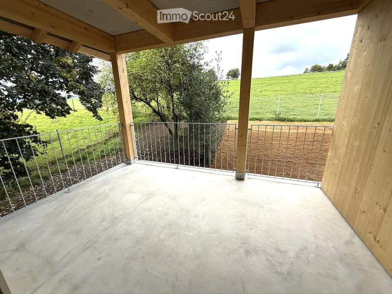 Wooden-framed balcony with metal railing, overlooking a green field and trees.