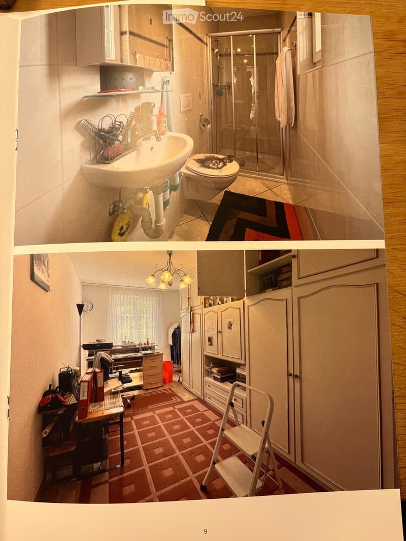 The image shows a small, furnished room with a sink, toilet, shower, and cabinet. The room includes a chair, table, and various personal items, indicating it is used as a living space.