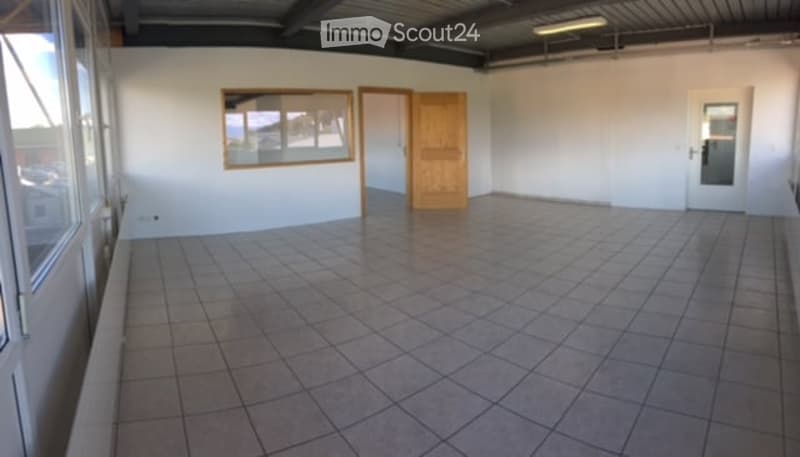 Empty room with tiled floor, white walls, large windows, and a wooden door.