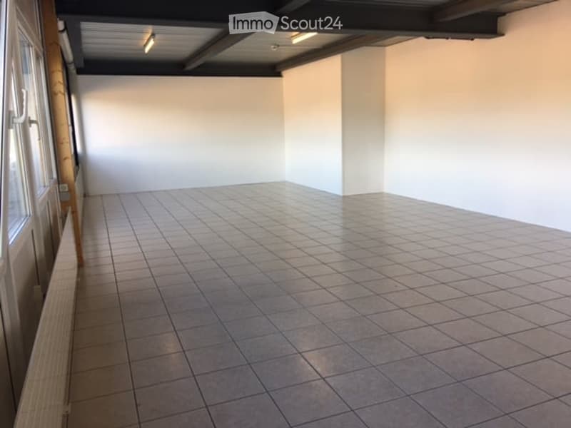 Empty room with tiled floor and white walls, featuring a window on one side and exposed ceiling beams.