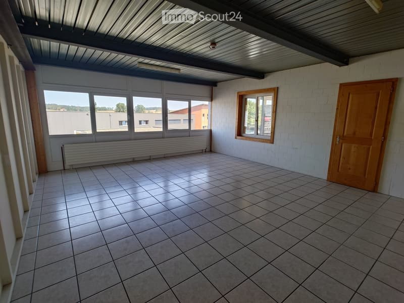 Empty room with tiled floor, white brick walls, large windows, and a wooden door.