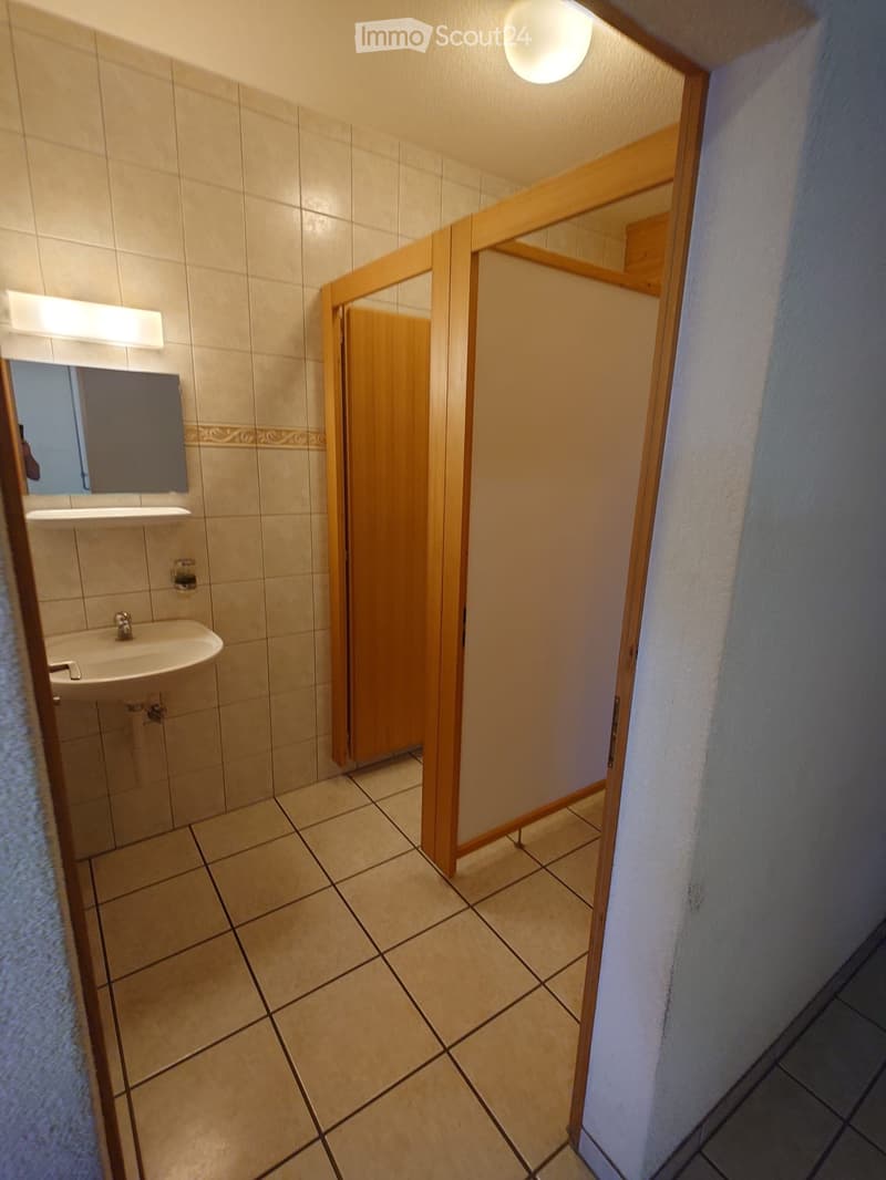 Bathroom with beige tiled walls and floor, a sink with a mirror above it, and a wooden shower stall with a glass door.