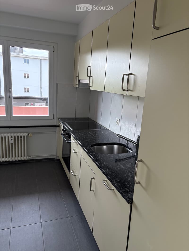 Modern kitchen with white cabinets, dark granite countertop, stainless steel sink, and built-in oven. Features a window with a view of a building.