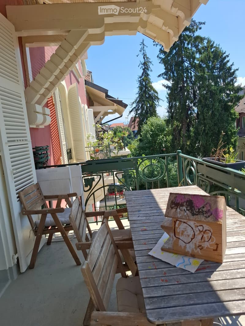 Balcony with wooden table, two wooden chairs, and a colorful painting on the table.
