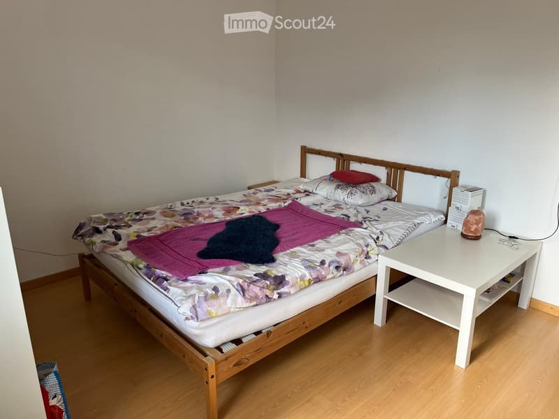 A small bedroom with a wooden bed, a white side table, and a patterned bedspread.