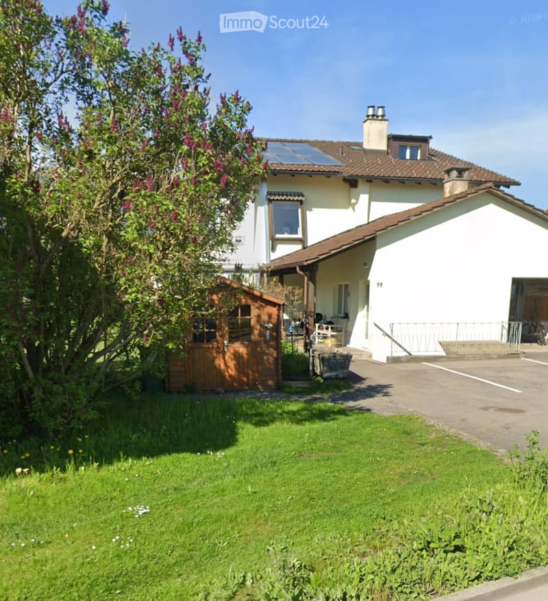 Two-story house with white walls, brown tiled roof, solar panels, garage, and small wooden shed in the garden.