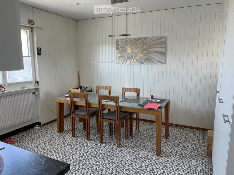 Dining room with a glass-top wooden dining table, four wooden chairs, a modern abstract painting, and a radiator under the window.