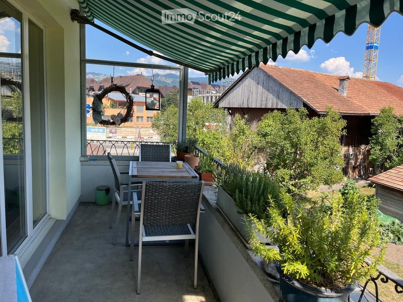Balcony with a striped awning, a small table with two chairs, potted plants, and a decorative wreath hanging on the wall.