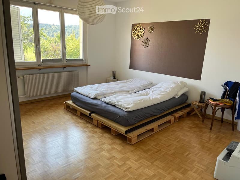 Bright bedroom with wooden flooring, a raised platform bed, large windows with a scenic view, and decorative wall art.