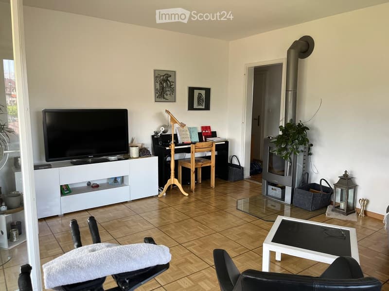 A modern living room with a fireplace, a large TV, a desk with a laptop, a coffee table, and a comfortable sofa.