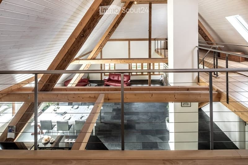 Open-plan living and dining area with exposed wooden beams, modern furniture, and a glass railing overlooking a lower level.
