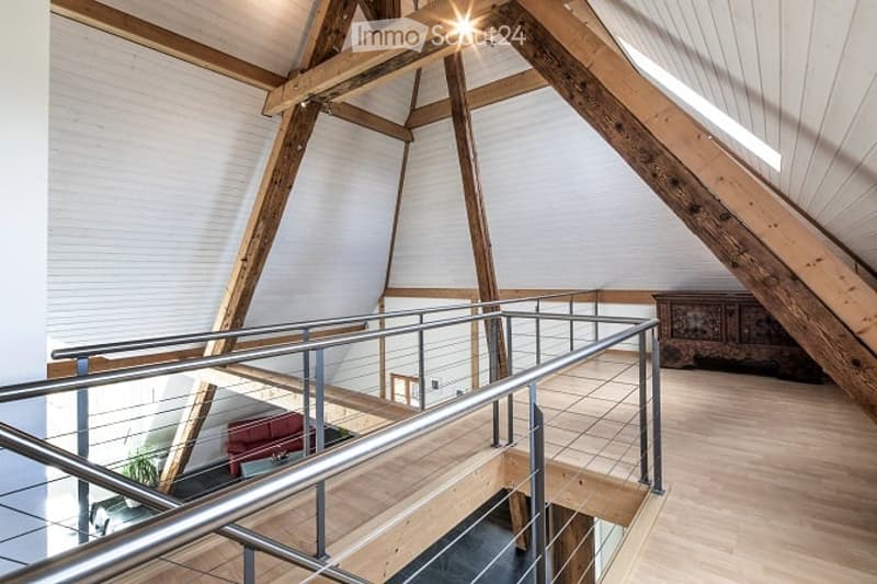 Loft-style interior with exposed wooden beams, modern metal railing staircase, and a red sofa in the background.